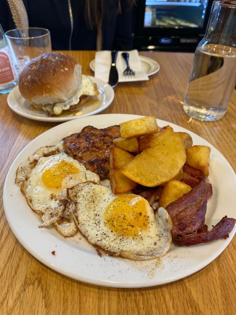 Breakfast plate with eggs, bacon, sausage, an potatoes with a breakfast sandwich in the background at Fat Rabbit in St. Catharines