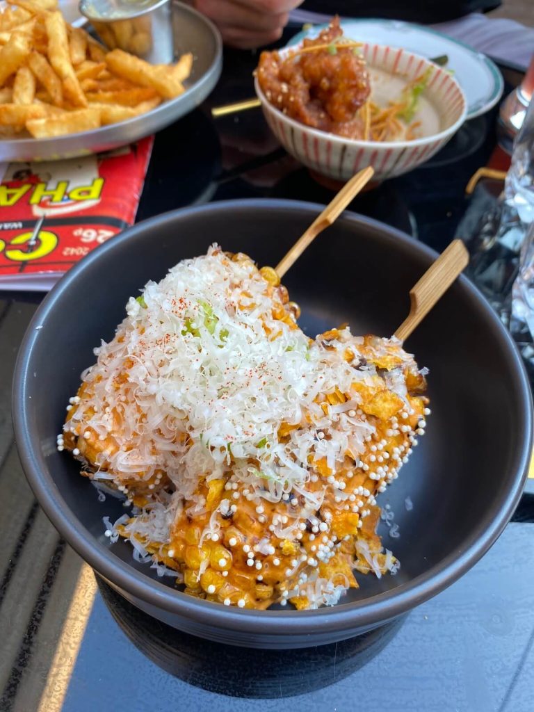 Bowl with two pieces of hipsy corn covered in Korean chili powder, chili aioli, puffed rice, and fresh parmesan cheese at Pharmacii in St. Catharines