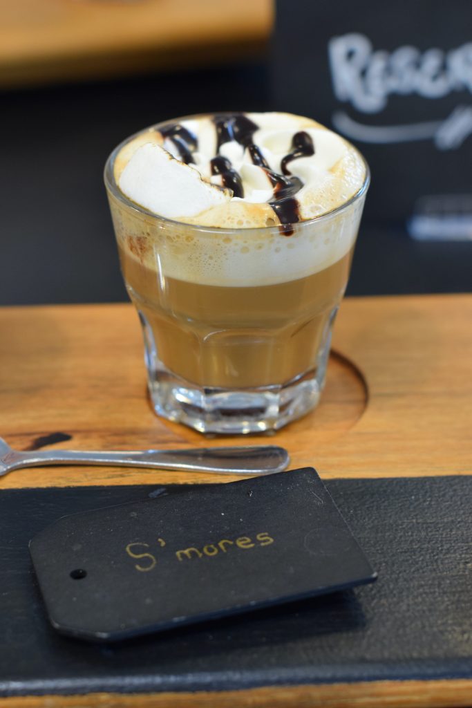 Glass filled with s'mores coffee with foam, chocolate, and a marshmallow on top. Part of the coffee flight at Junction in Niagara-on-the-Lake